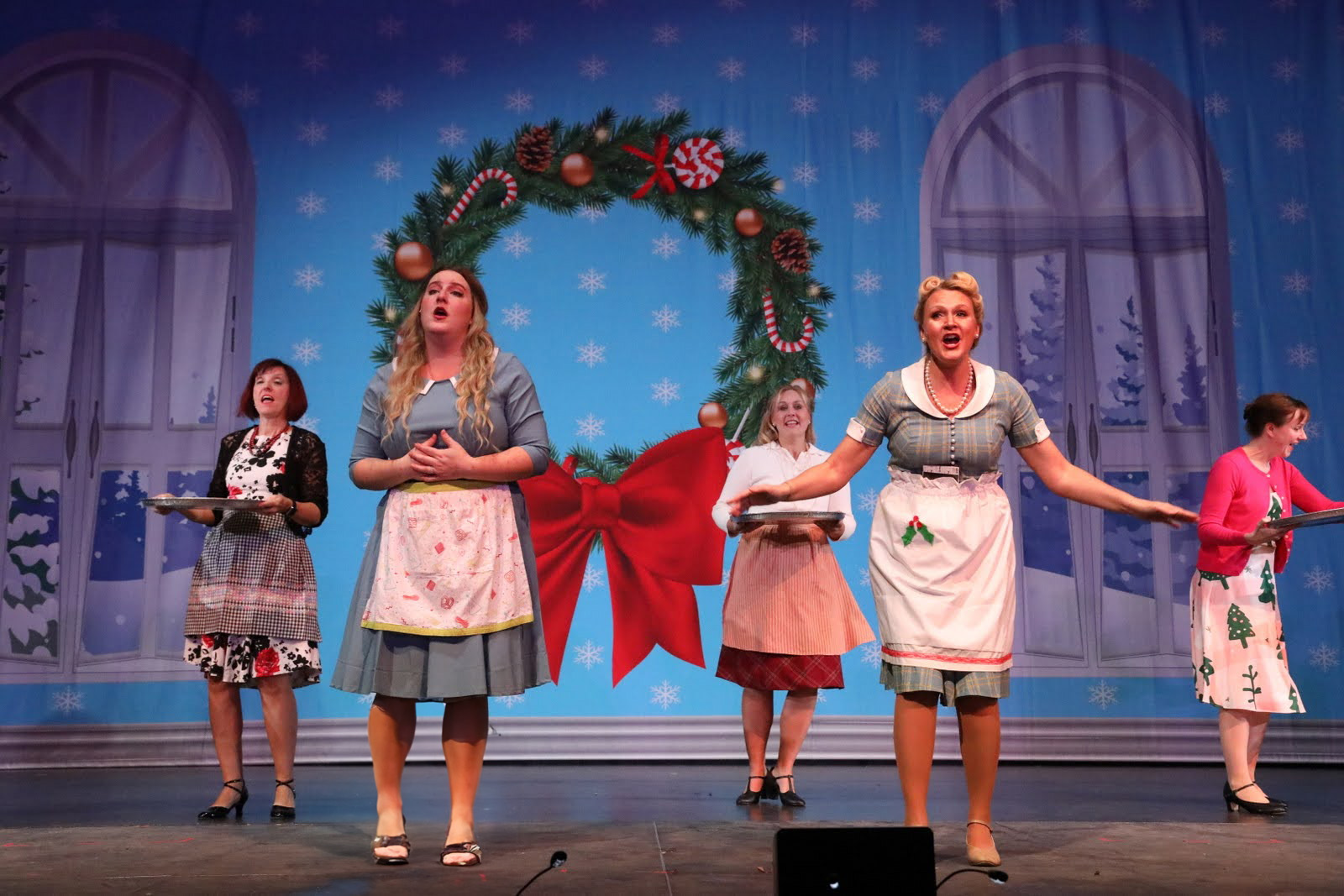 Five women dance in front of a indoor holiday drop.